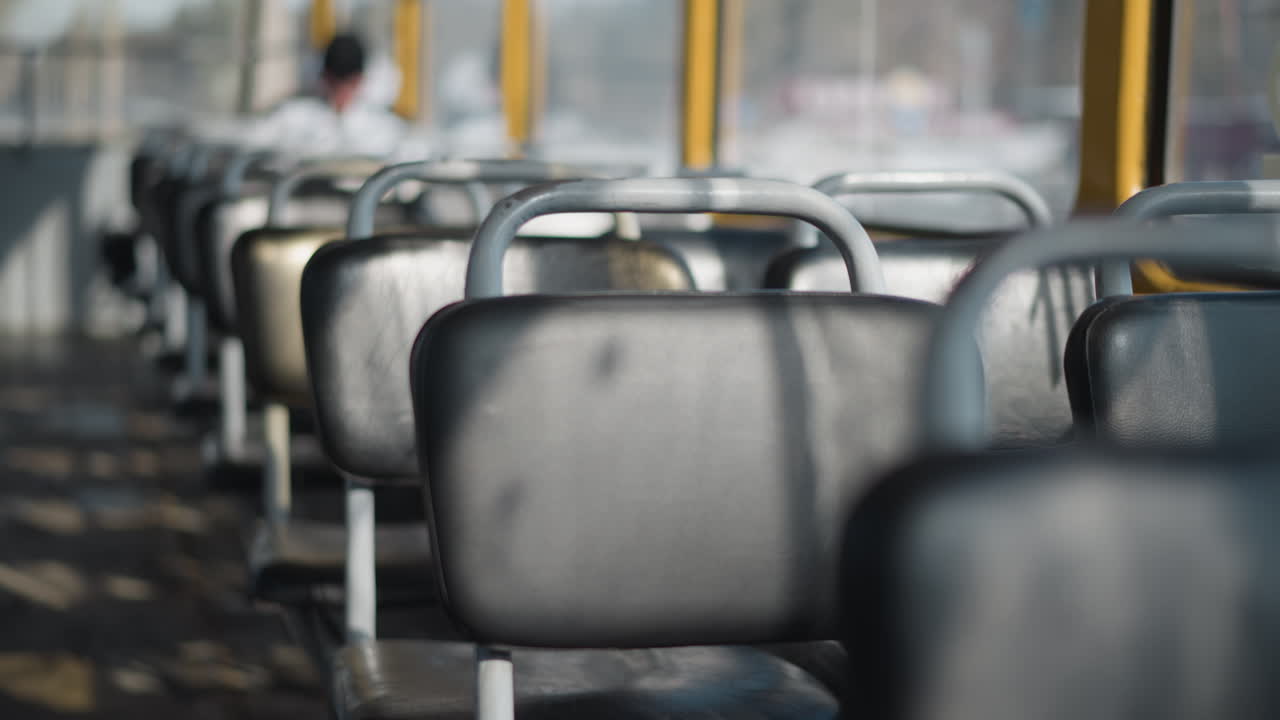 close up empty rubber seats on bus while sun rays slice across aisle, long shadows ripple over worn floor, glints on metal frames and vinyl cushions, quiet midday ride mood