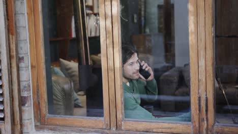 Happy-caucasian-man-talking-on-smartphone-sitting-by-window-at-home,-slow-motion
