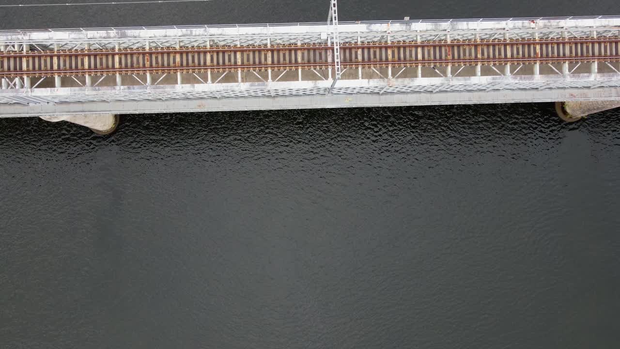 4K drone overhead shot (top-down) of the metal railway bridge over the dark Minho River, showcasing the tracks and geometric structural patterns, Tui, Galicia, Spain