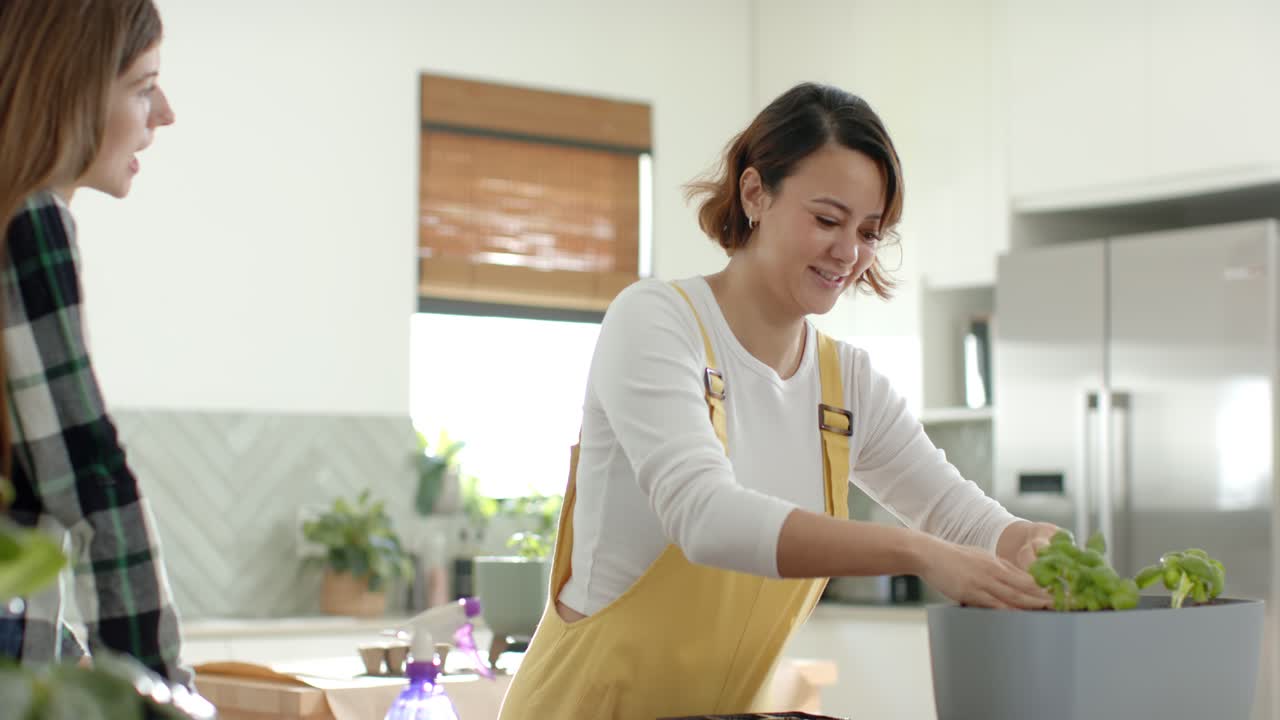 自宅で、多様な女性たちが、黄色い服の女性がトレーから植物を取り出して灰色のプランターに植えているのを見ている。