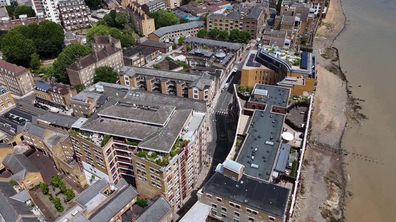 Aerial view of riverside streets and converted warehouse buildings beside the tidal foreshore, with a boat passing on the water