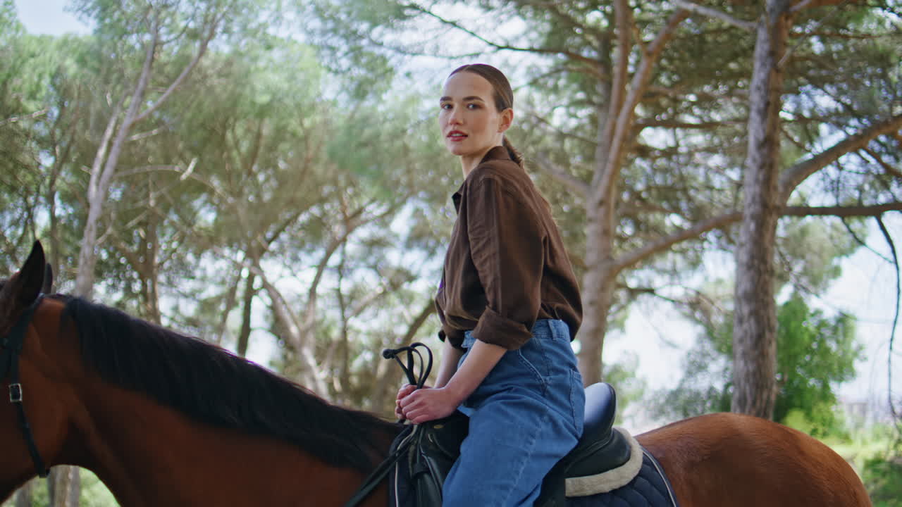 Attentive cowgirl horseback riding green wood closeup. Equestrian sitting horse