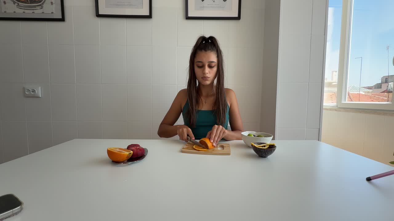 Mujer joven pelando y cortando una naranja fresca.