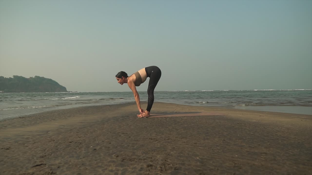 el saludo al sol plantea la práctica de asanas de yoga en la playa por una mujer caucásica morena