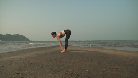 sun salutation pose yoga asana practice on beach by brunette caucasian woman