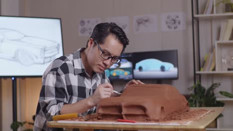 asian man automotive designer smiling to the camera while working on the sculpture of car clay in the studio