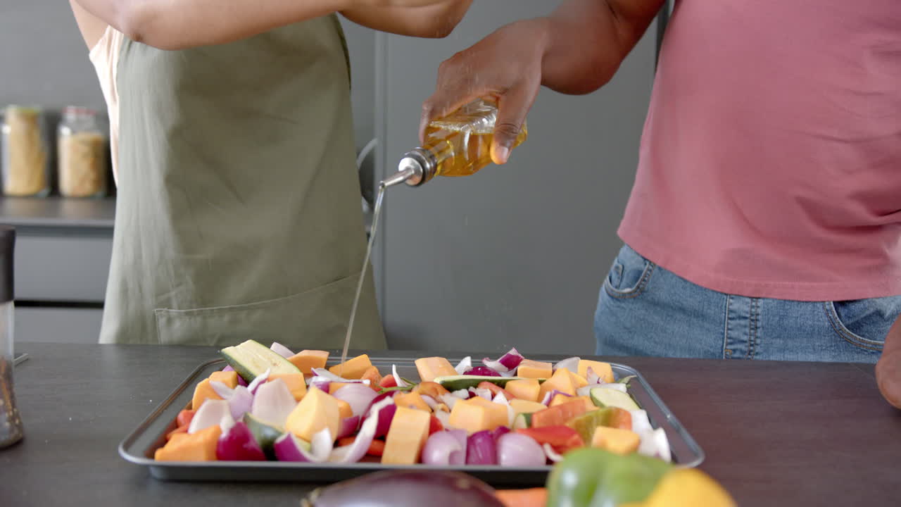 Preparing vegetables, couple seasoning and drizzling oil on baking tray in kitchen