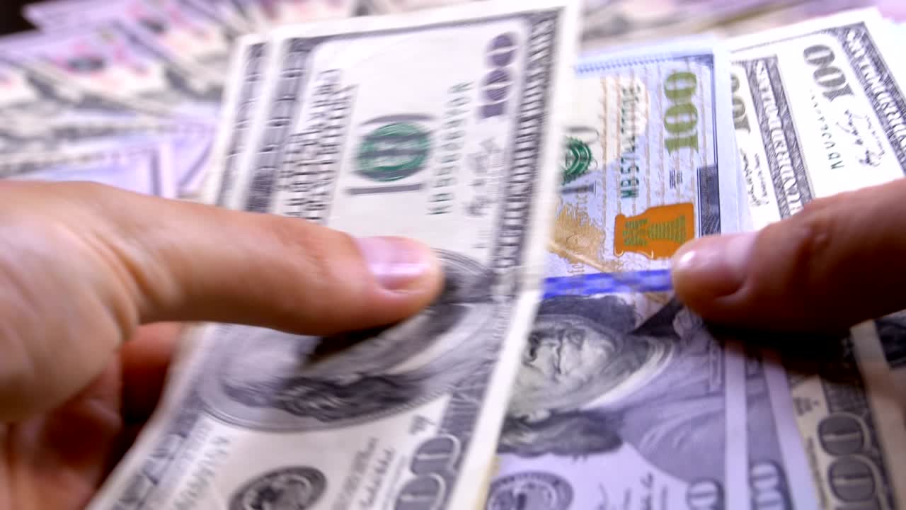 las manos de los hombres sostienen un montón de dólares estadounidenses contra el fondo de dinero giratorio