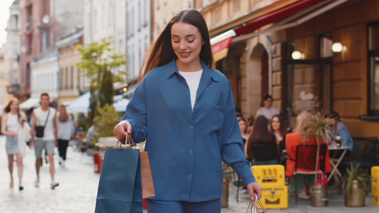 Happy young woman shopaholic consumer after shopping sale with full bags walking in city street