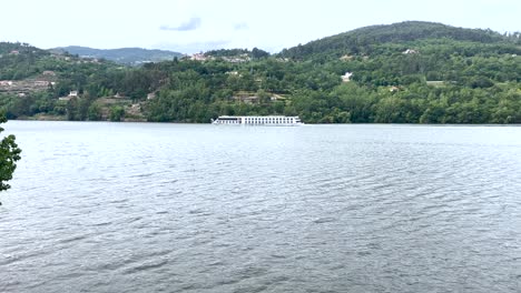 Touristic-Cruise-ship-boat-over-river-Tagus-with-green-hills-in-background,-Portugal