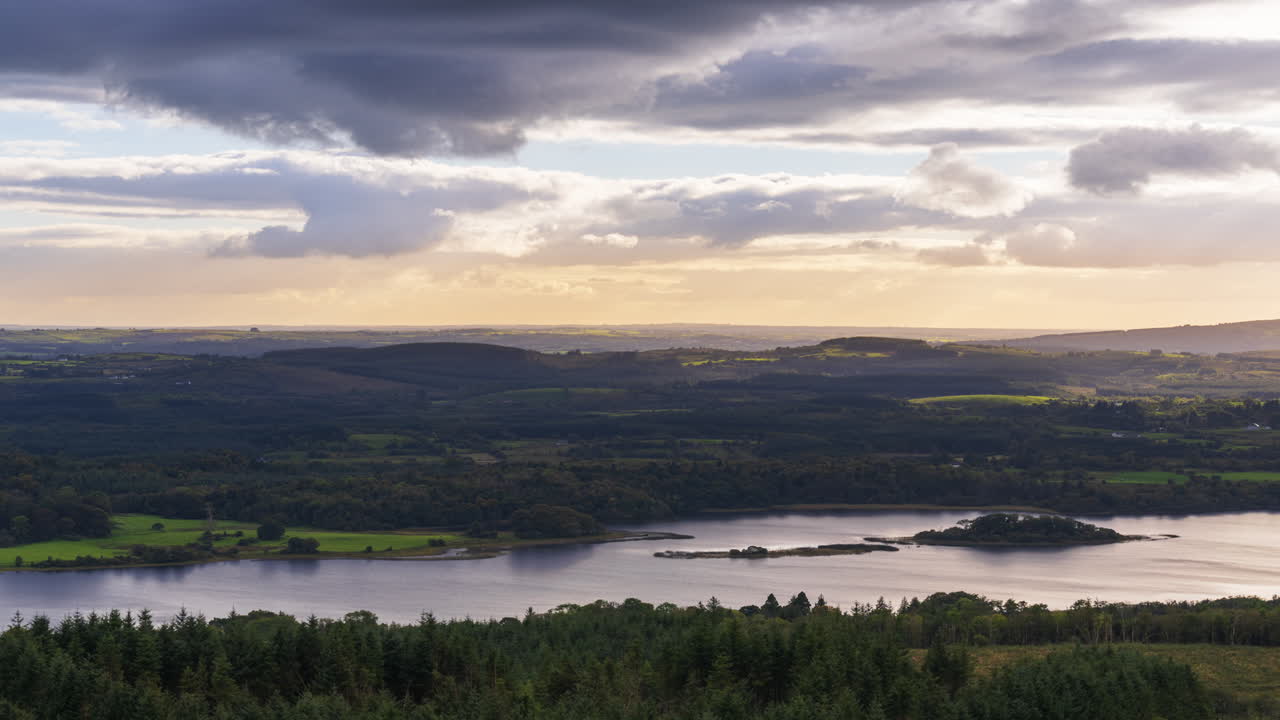Time lapse of rural farming landscape with lake, forest and hills during a cloudy evening sunset viewed from above Lough Meelagh in county Roscommon in Ireland