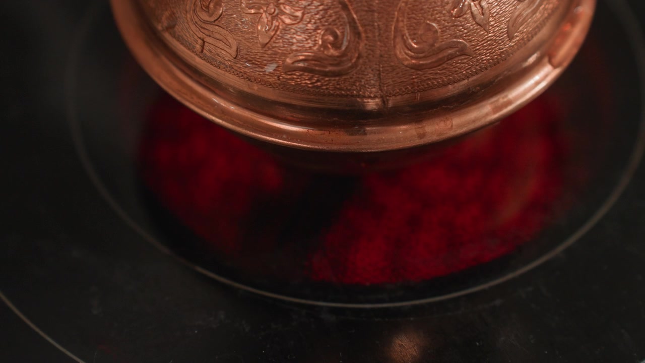 Ornate cezve over red burner closeup brewing motion with bubbling coffee, copper embossing, glossy cooktop reflection, rising steam, ritual tension, artisan barista vibe for coffee lover