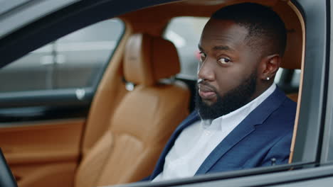 Closeup-businessman-looking-at-camera-at-car.-African-man-smiling-in-luxury-car