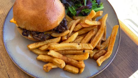 tasty cheeseburger with french fries and salad on a plate by the sand, beach restaurant, 4k shot