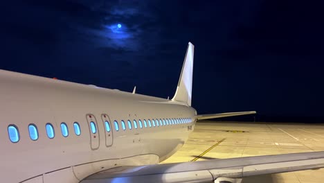 night view of parked airplane on airport apron with white body showing fuselage wing engine and tail with moon in background