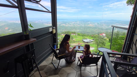hillside kokol cafe on kokol hill - mother and daughter sit by the window with a picturesque view of kota kinabalu. dolly-out shot
