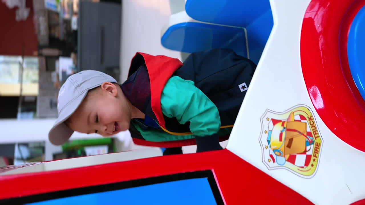 Excited Caucasian baby boy playing inside the toy car. Happy kid jumping and smiling to camera. Vertical screen.