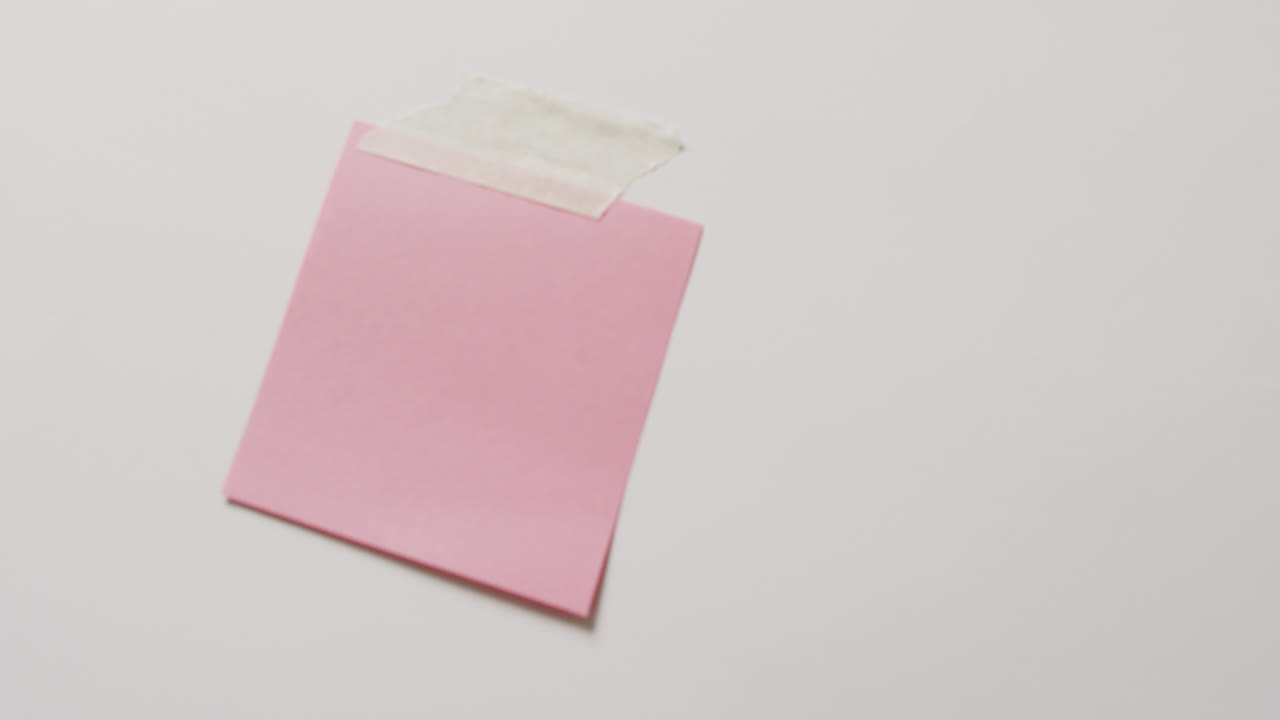 Video of close up of pink memo note with copy space taped to white background