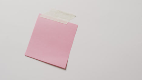 Video-of-close-up-of-pink-memo-note-with-copy-space-taped-to-white-background