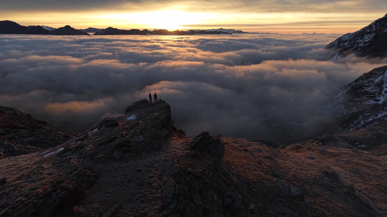 Sorvolo aereo su escursionisti che si godono il bagliore dell'alba sopra l'inversione delle nuvole nelle Alpi svizzere con una panoramica verso l'alto delle montagne e del cielo colorato