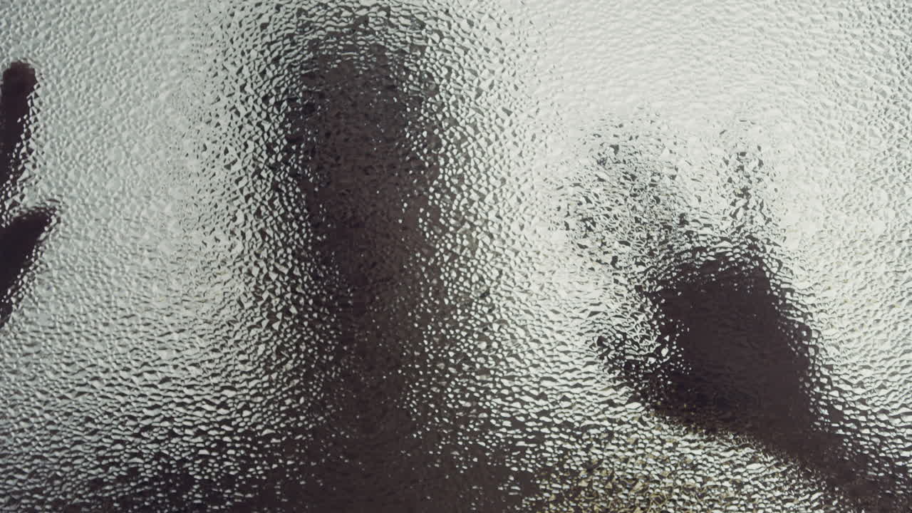 A female silhouette behind the frosted window touches the glass slowly