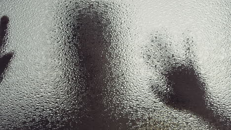 a female silhouette behind the frosted window touches the glass slowly