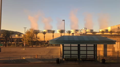 POV-shot-driving-past-smoking-chimneys-of-a-power-plant,-during-sunset