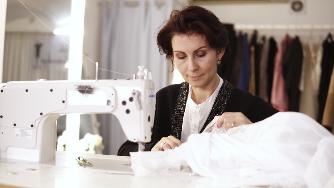 retrato de una costurera adulta que trabaja en una máquina de coser, trabajando en un vestido blanco hecho a mano.