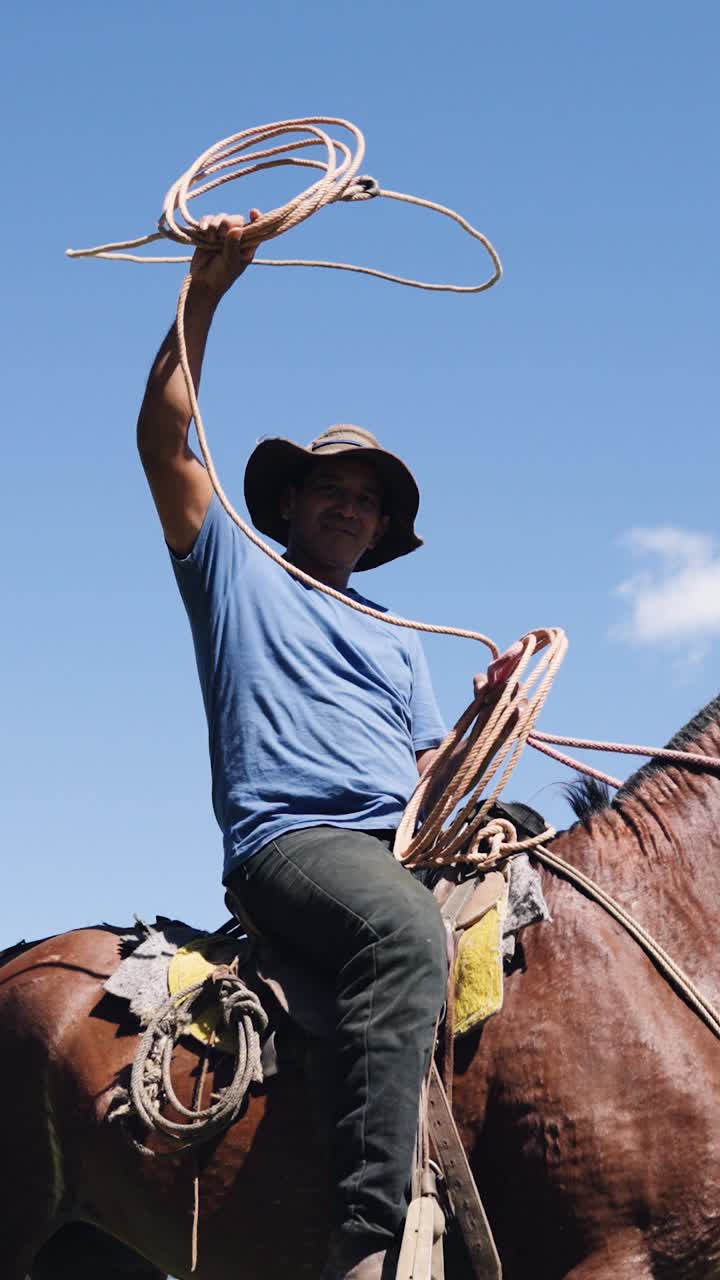 Vaquero a caballo haciendo girar un lazo contra el cielo azul.