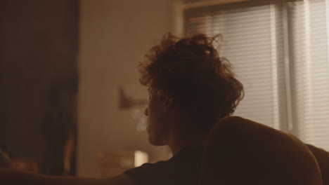 melancholic young man smoking cigarette in warmly lit room