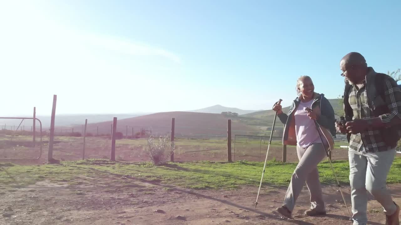 pareja de ancianos afroamericanos con mochilas caminando en la naturaleza soleada con espacio de copia, cámara lenta