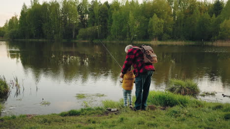 rest in shore of forest lake grandfather and grandson are fishing from coast rear view