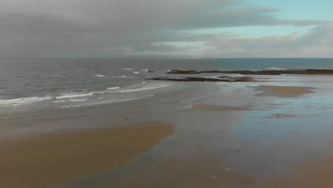 Disparo-De-Drone-Moviéndose-Sobre-Pequeñas-Olas-Rodando-En-La-Costa-Escocesa