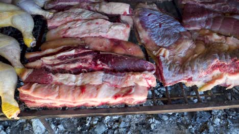 raw argentinian chicken and beef asado grilling over smoky embers