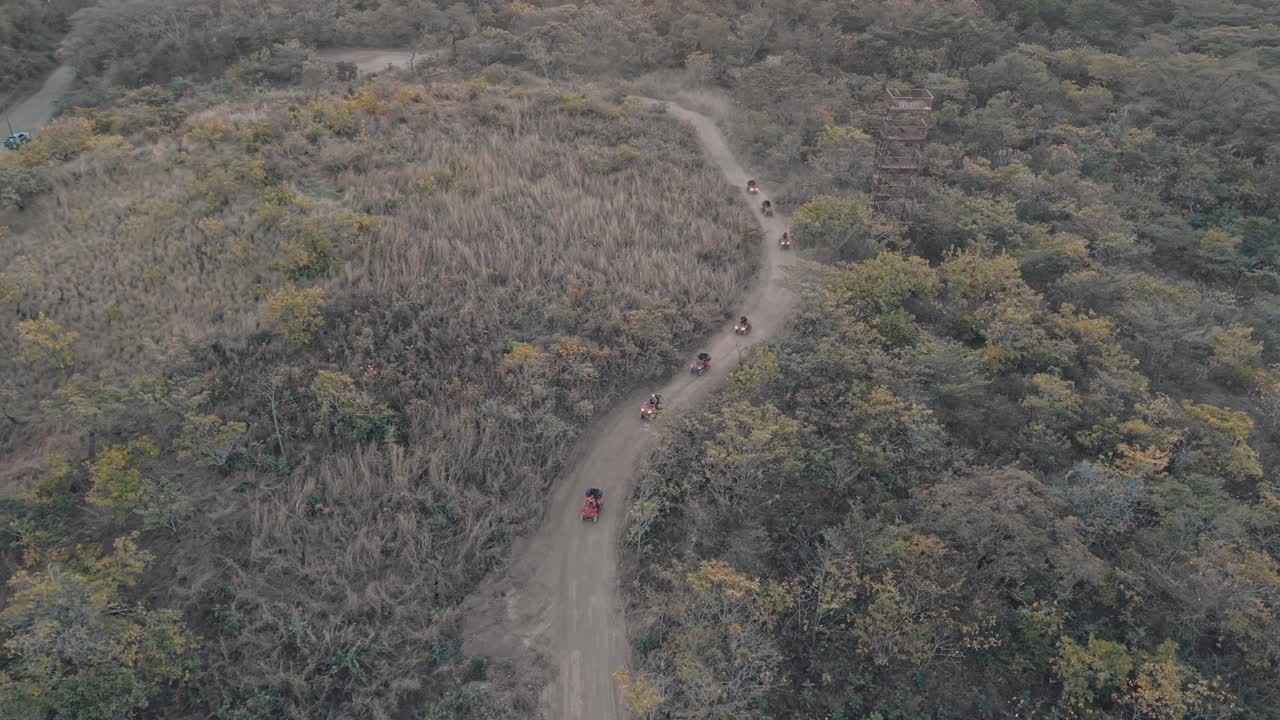 Overhead zoom out of ATVs riding along a dirt road surrounded by dry forest in Costa Rica.