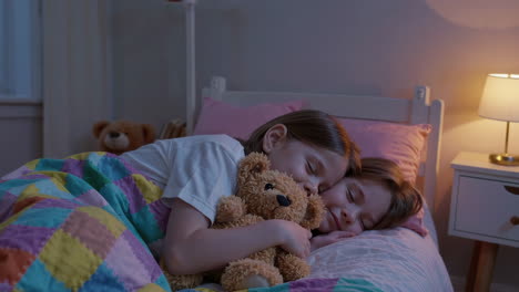 two young girls sleeping soundly with a teddy bear in a cozy bedroom