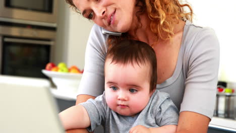 madre sentada con el bebé en el regazo usando una computadora portátil
