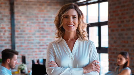 Portrait-Of-Smiling-Businesswoman-In-Office-With-Colleagues-Working-In-Background