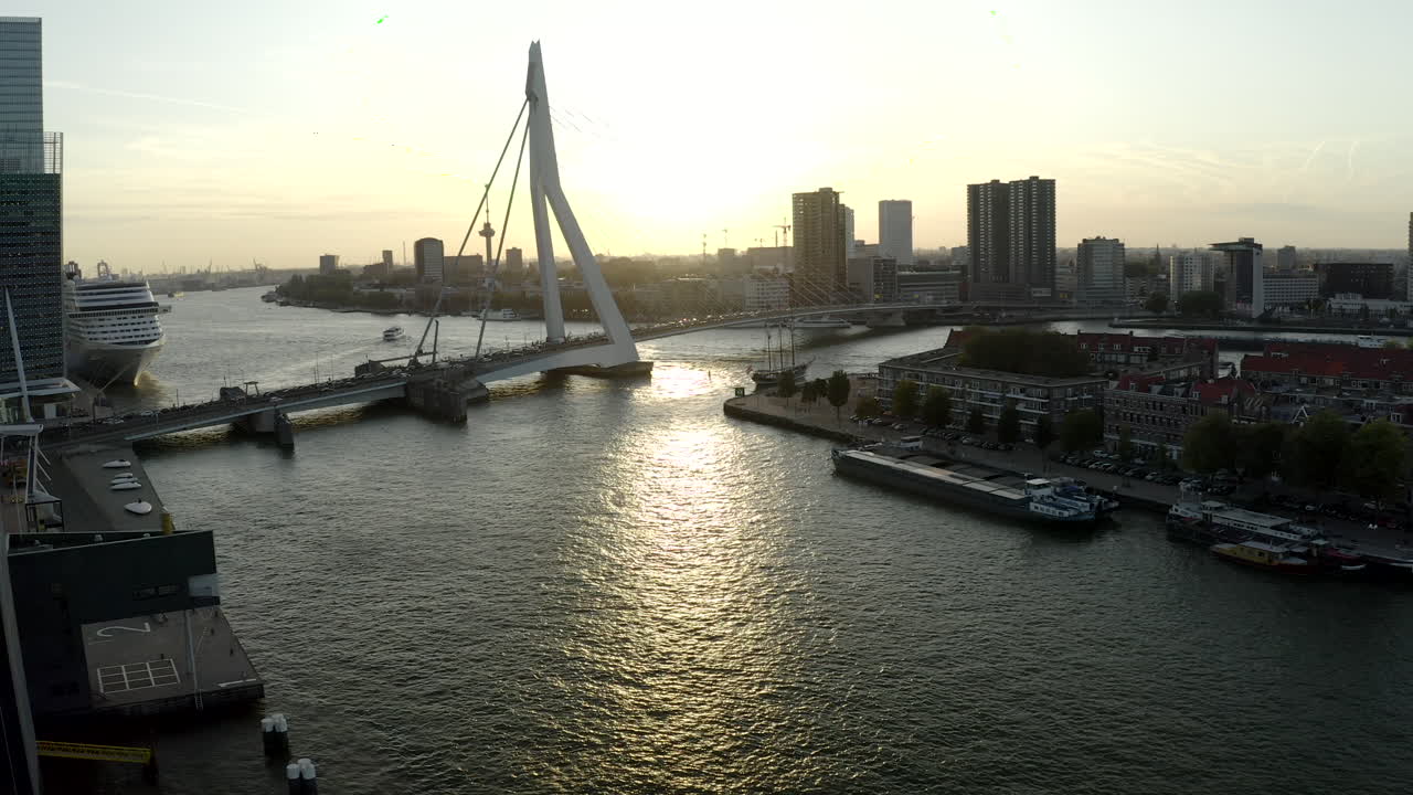 Toma de dron ascendente de Róterdam, Holanda, desde el río Nieuwe Maas con vistas a Noordereiland y Erasmusbrug durante el atardecer y un crucero atracado a la izquierda