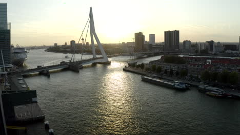 Aufsteigender-Drohnenschuss-Von-Holland---Rotterdam-Vom-Fluss-Nieuwe-Maas-Mit-Blick-Auf-Noordereiland-Und-Erasmusbrug-Während-Des-Sonnenuntergangs-Und-Einem-Kreuzfahrtschiff,-Das-Links-Angedockt-Ist