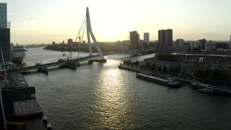 ascending drone shoot of holland - rotterdam from river nieuwe maas with view of noordereiland and erasmusbrug during sunset and a cruise ship docked on left