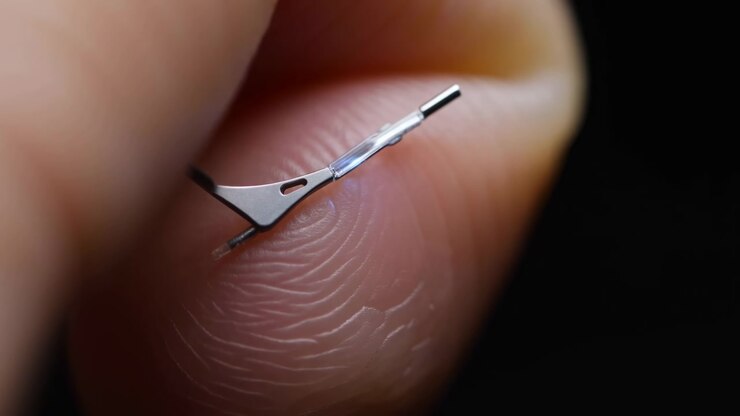 Extreme close-up reveals a miniature silver part balanced on textured fingertip ridges as intermittent blue illumination flickers through the transparent sleeve in shallow focus.