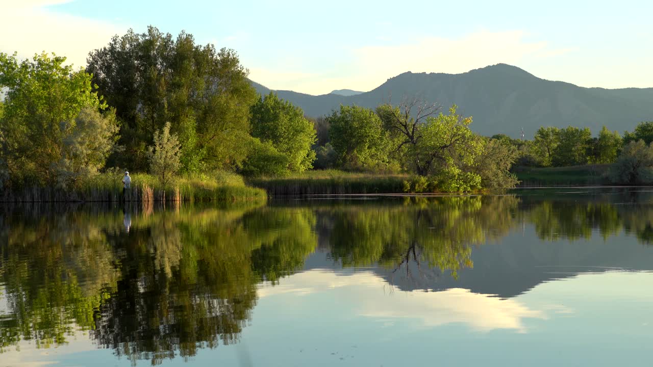Mann som fisker ved en innsjø med vakker fjellutsikt og refleksjon