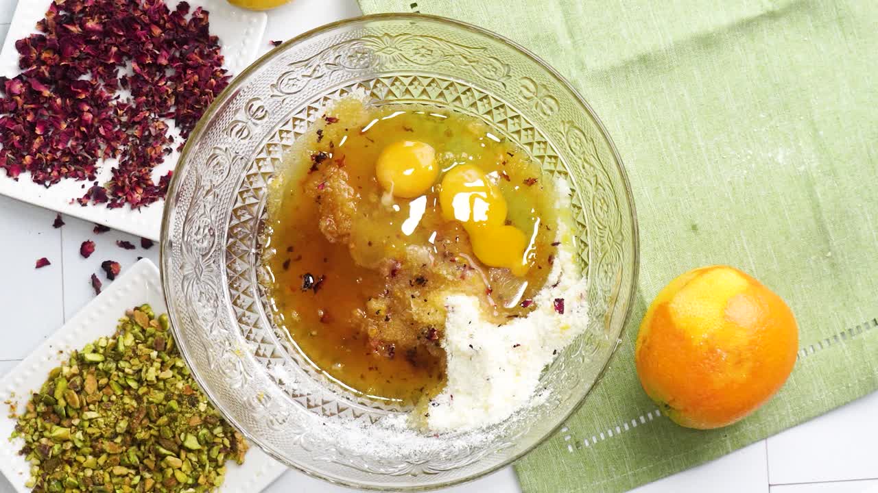 Baking a dessert called Persian Love Cake made with rose petals and pistachios. Cake with white glaze frosting. Adding milk or heavy cream to a bowl. Beautiful cake for tea time or celebration