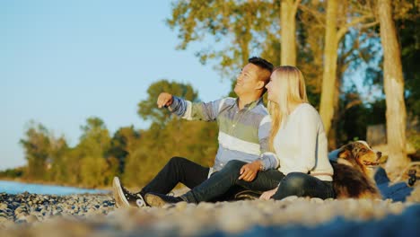 a young couple is resting on the lake, next to them is a dog