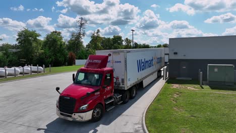 aerial orbit shot of red walmart truck with reverse gear at industrial warehouse. sunny day with clouds in industrial area of america.