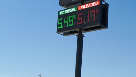 gas station pump prices high over 5 five dollars per gallon 5.17 unleaded 5.49 diesel tall outdoor sign flickering on a super hot scorching sunny blue sky summer day zooming out and panning down