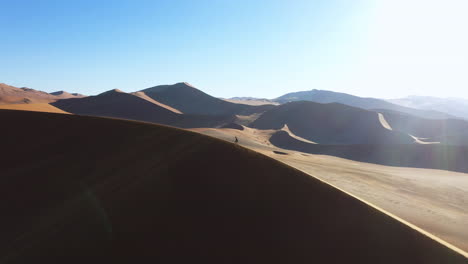 Man-hiking-on-top-of-a-dune,-sunny-day-in-the-Namib-desert-of-Namibia---Aerial-view