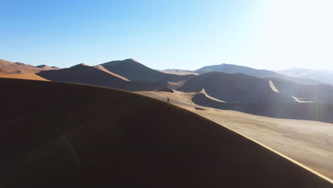 man hiking on top of a dune, sunny day in the namib desert of namibia - aerial view