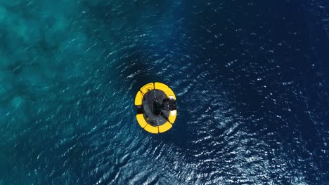 Drone-top-down-shot-on-yellow-mooring-buoy-in-deep-blue-Caribbean-ocean,-small-waves-and-wind-ripples